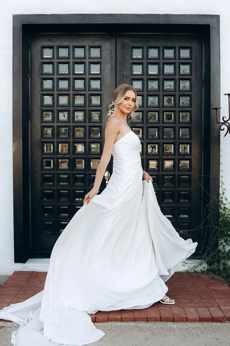 Model is wearing a soft A-line chiffon gown with a strapless sweetheart neckline, gathered draping at the bodice, and a cascading back detail.