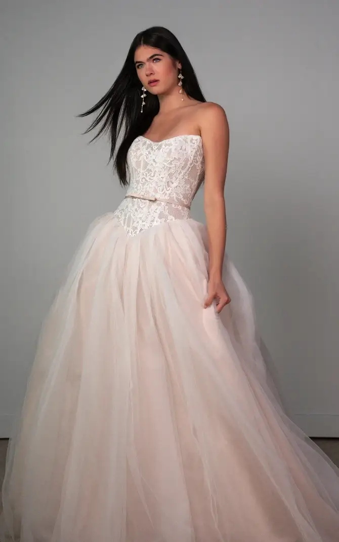 Model is wearing a blush pink strapless ball gown wedding dress with a basque waist and tulle skirt