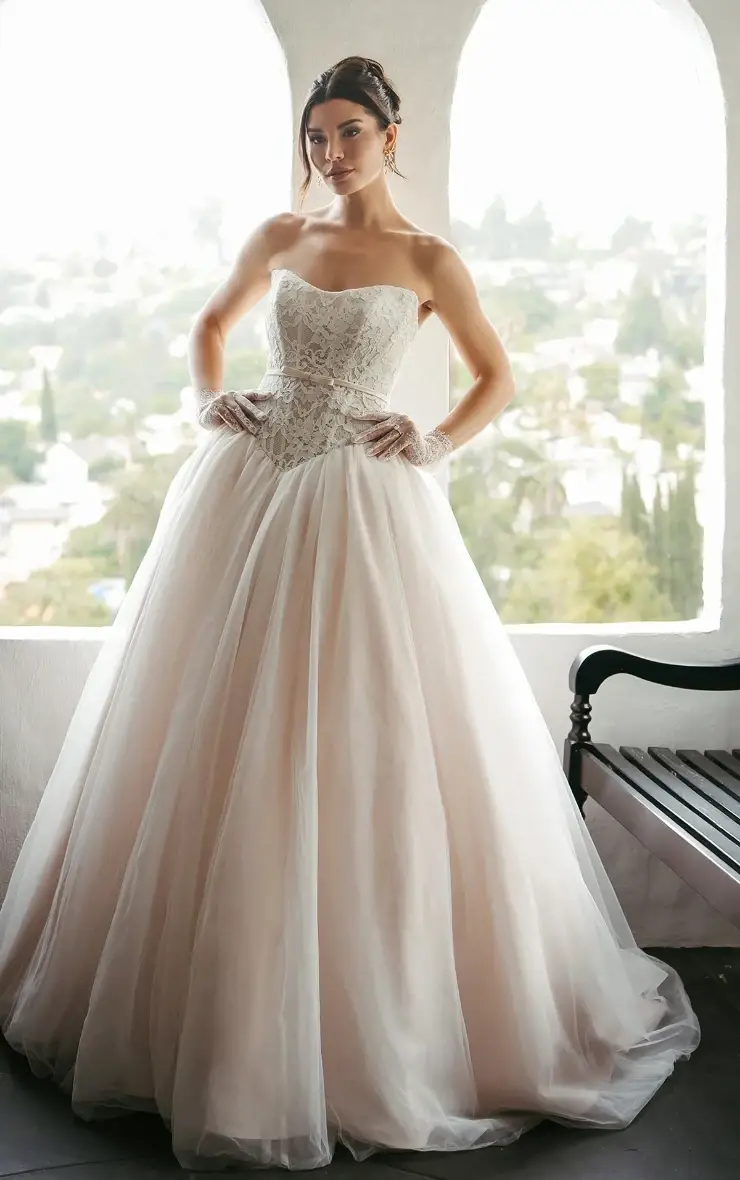 Model is wearing a blush pink strapless ball gown wedding dress with a basque waist and tulle skirt
