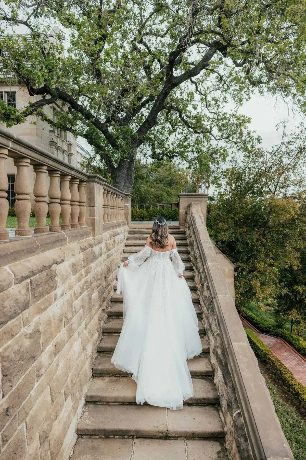 Model is wearing an a-line wedding dress with detachable off the shoulder blouson sleeves and a long train