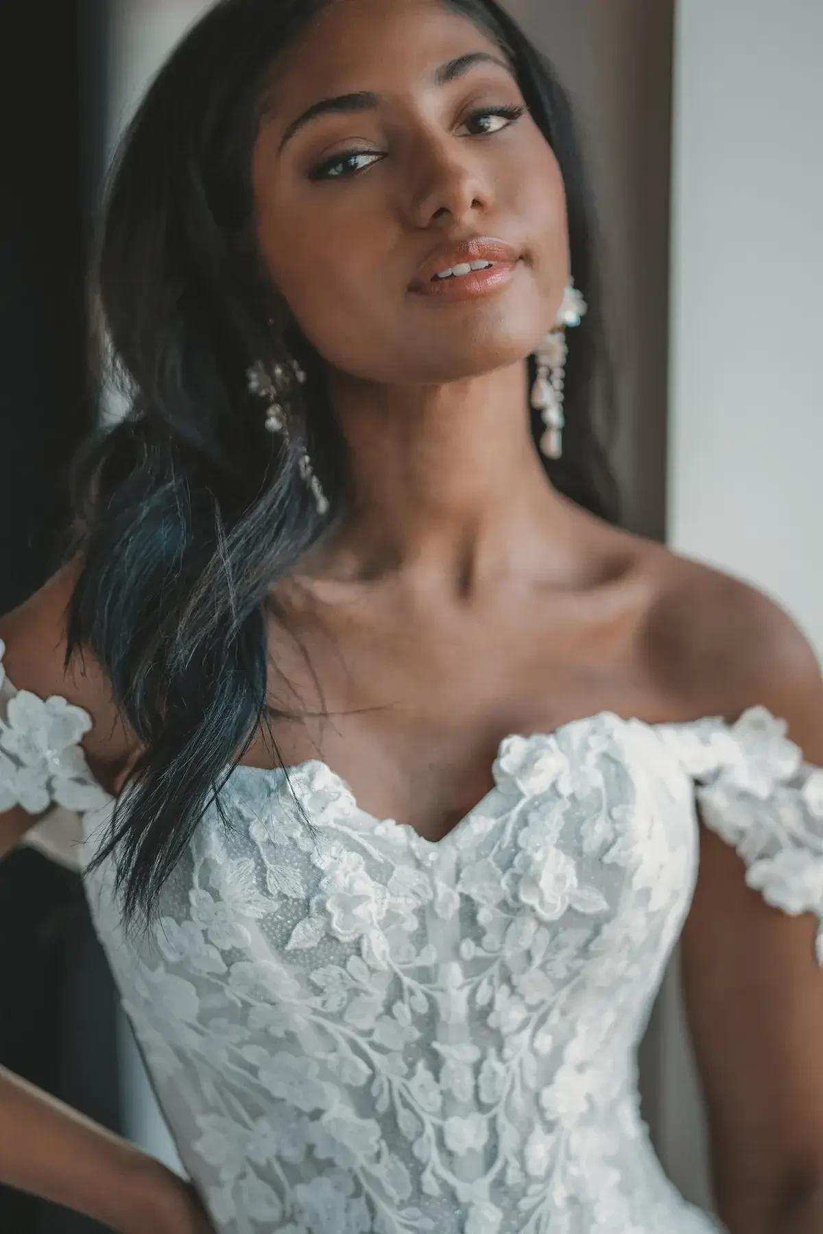 Model is wearing a princess wedding dress with lacy off the shoulder straps and a corset bodice with floral lace accents