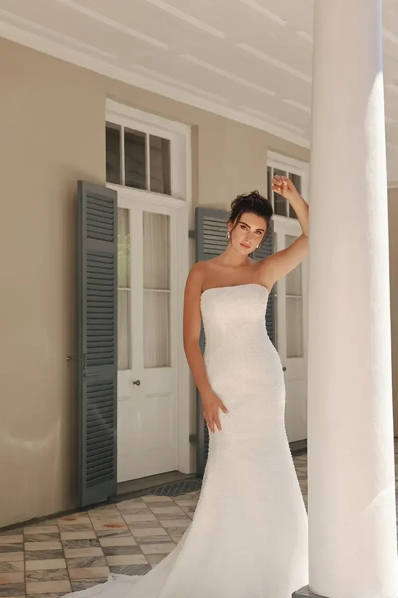 Model is wearing a sleek wedding dress with a trumpet skirt and embellished pearl tulle