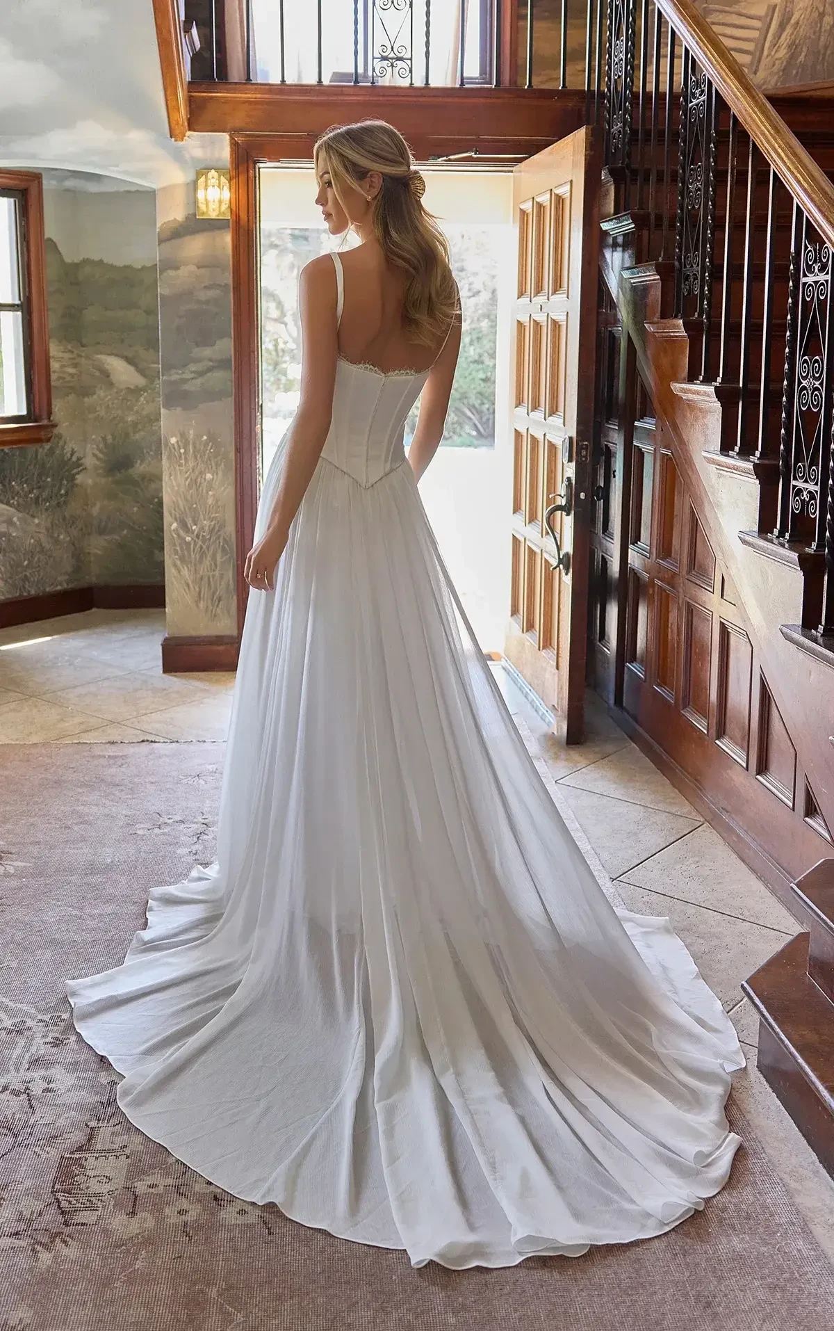 A woman in an elegant, flowing white wedding dress stands in a warmly lit hallway. She faces an open wooden door, evoking a sense of new beginnings.